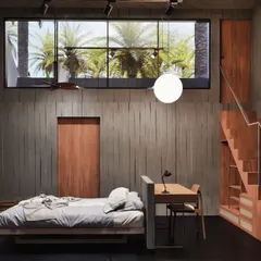 This two-tiered bedroom is a self-contained retreat designed to connect with the surrounding farmland. A large window frames the view of palm trees, while a cozy bay window seat offers a place for quiet reflection. The material palette of wood-shuttered concrete and timber adds warmth and texture.