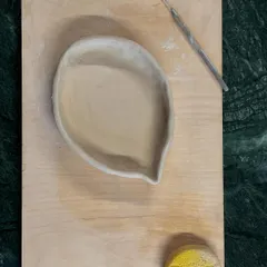 A freshly hand-built piece, a leaf-shaped dish, resting on a board with its tools. This is the beginning of its journey.