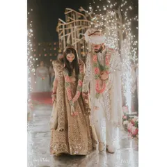 A moment of quiet connection amidst the grand celebration. The couple walks hand-in-hand, framed by the sparks of cold pyros, their path illuminated as they begin their life together.