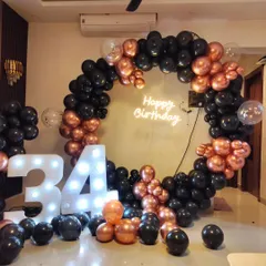 A stylish 34th birthday party with a black and rose gold theme, featuring a full circular balloon arch and large light-up marquee numbers.