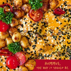 A vibrant close-up of the Smoked Paprika Piri-Piri Hummus. You can see the rich texture, toasted chickpeas, fresh tomatoes, and sesame seeds that make every scoop a flavor explosion.