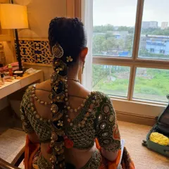 A side profile of an intricate bridal braid, showcasing how the hairstyle is constructed to complement the bride's posture and outfit. The mix of flowers and jewellery adds layers of texture and elegance.