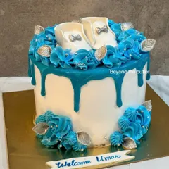 It's a boy! This welcome cake for baby Umar features a beautiful blue drip, blue buttercream rosettes, and tiny, handcrafted white fondant baby shoes.