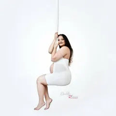 A graceful portrait of an expectant mother seated on an aerial silk swing. This pose highlights her strength and the beauty of her pregnancy in a simple, elegant way.