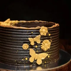 A minimalist take on a chocolate cake. This design features a textured dark chocolate ganache, decorated simply with delicate gold butterflies, flowers, and a sprinkle of gold dust.