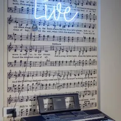 We incorporated the children's passion for music with this piano nook, featuring a wallpaper of sheet music and a "LIVE" neon sign. It's a fun, energetic corner that truly brings the room to life.