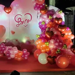 A close-up of our romantic Valentine's Day photo booth. The setup features a "Love" backdrop and a lush balloon garland in shades of red, pink, and orange, accented with heart-shaped foil balloons.