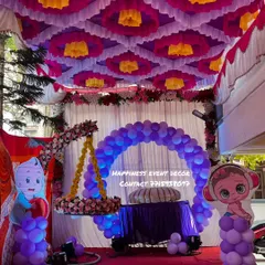 A full view of the naming ceremony stage with the hanging cradle. The entire area is decorated with a colorful tent-style ceiling, a balloon arch, and cute baby cutouts, making it a complete package.