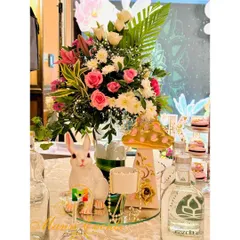 A whimsical centerpiece for a fairy-themed party, combining a fresh floral arrangement with a cute bunny figure and a painted mushroom prop.