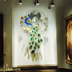 The peacock wall clock shown under focused lighting, which highlights the texture and shadows of the metalwork, enhancing its artistic quality.