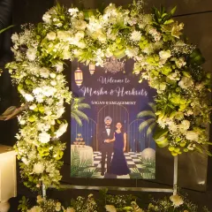 A beautiful welcome sign for an engagement ceremony, personalized with the couple's names and an illustration, framed by a fresh floral arch.