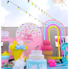 A full view of the ice cream-themed party setup. It includes a multi-tiered cake display, a giant ice cream cone, a sprinkle-covered backdrop, and a pastel rainbow arch, creating a complete visual feast.