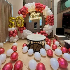 An elegant 50th anniversary decoration for an at-home celebration. This setup is built around a circular frame with a chrome red and white balloon arch, a central 'Happy Anniversary' neon sign, and large '50' foil balloons.