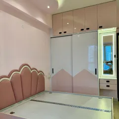 A beautiful bedroom for a princess. The design includes a custom scalloped headboard, pink and white sliding wardrobes, and a matching dressing table with a lit mirror.