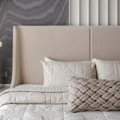 A close-up on a masterfully crafted bed, featuring a lumbar cushion with a woven leather texture. This single accent piece adds a powerful tactile element to the serene, neutral bedding, showcasing how a small detail can make a significant impact.