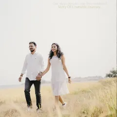 A bright and happy shot of a couple in modern-casual white outfits, walking through a sunlit field.