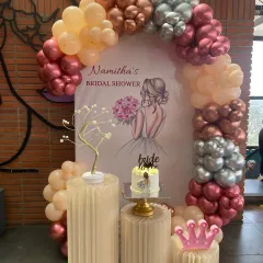A chic and modern bridal shower setup. This design features a stylish balloon arch in metallic and pastel tones, a personalized backdrop, and elegant plinths for the cake and decorative props.