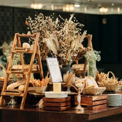 A rustic bread and cheese station, complete with a variety of artisanal loaves, breadsticks, and a warm cheese fondue. The wooden crates and dried flowers add to the charming, rustic aesthetic.