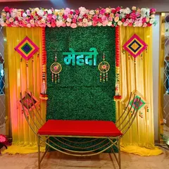 Here is a recent Mehndi decoration I did, featuring a green grass wall backdrop with a "Mehndi" sign in Hindi. The look is completed with colorful hangings and a red bench for the bride.