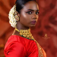 A classic portrait that emphasizes the model's striking features and the beauty of the South Indian bridal aesthetic. The warm background complements the red saree, making the entire image pop with color and life.