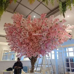 This stunning, large-scale artificial pink cherry blossom tree acts as a magnificent centerpiece in a cafe, offering a vibrant and unique ambiance that attracts customers.