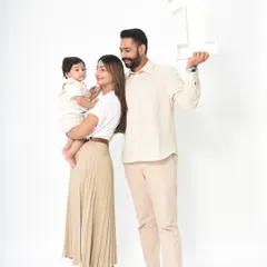 A clean and classic first birthday portrait. The family stands together against a simple white background, with the father holding a large number '1' prop to celebrate the big day.