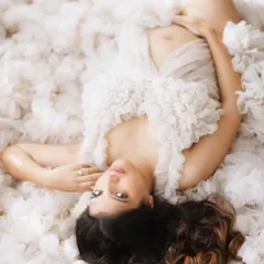 Lost in a sea of soft white ruffles. This artistic pose and gown create a feeling of pure softness and vulnerability, highlighting the delicate beauty of the maternal form.