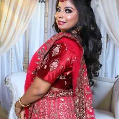 A side profile of the red bridal lehenga look, showing the intricate hairstyle with soft waves and crimped texture. The dupatta is draped elegantly over her shoulder.