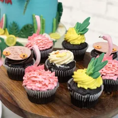 A close-up of the tropical-themed cupcakes, some with pink flamingo toppers and others with yellow pineapple frosting.