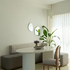 This minimalist dining nook is designed for quiet meals. A built-in bench with plaid upholstery is paired with a simple pedestal table and a classic wooden chair. The organic-shaped mirrors on the wall add a touch of artistry and reflect light.