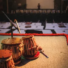 The stage is set for a Courtyard Baithak. The floor seating, the marigold flowers, and the waiting tabla create a sense of anticipation for the intimate musical evening ahead.