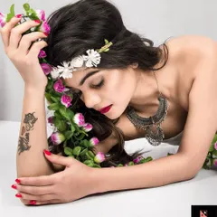 A serene pose from the 'Gaia' concept shoot. The model, adorned with a floral crown and garland, rests her head on her arm, embodying the peaceful and gentle spirit of the nature goddess.