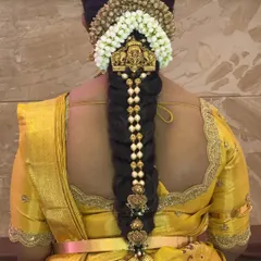 A traditional bridal braid that tells a story of love and culture. This style features a long, thick braid decorated with pearl-studded ornaments and finished with a classic kunjalam.