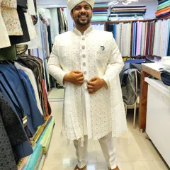A groom feeling confident and happy during his fitting session. He is wearing a custom all-white embroidered sherwani with a matching pagdi and juttis, an outfit designed to make a remarkable impression.