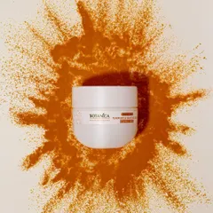 A dynamic overhead shot of a face cream jar with a burst of turmeric powder. This visually connects the product to its key natural ingredient.
