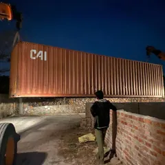 The container is precisely lowered into place, marking the foundational moment of the structure. This process requires careful planning and execution.
