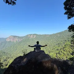 A trekker sitting on a rock with arms outstretched, enjoying the stunning valley view from Narasimha Parvatha.