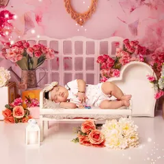 This baby is sleeping on a miniature white chaise lounge, set against a soft pink floral backdrop. The entire scene is filled with beautiful bouquets, creating a truly romantic portrait.