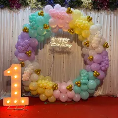 A beautiful pastel rainbow ring for a first birthday celebration. This circular arch uses soft shades of pink, yellow, mint, and lilac, with small gold accents and a neon 'Happy Birthday' sign. The large light-up '1' makes it clear what the special occasion is.
