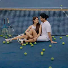 A relaxed moment on the tennis court, surrounded by tennis balls. This shot captures the fun and easygoing chemistry of the couple after a friendly match.