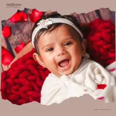 The purest joy in a single frame. This close-up from a newborn session highlights that beautiful, gummy smile, framed by a soft red knit blanket and delicate rose petals for an artistic and tender portrait.