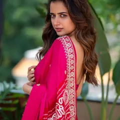 "ಯಾವ ಕವಿಯ ಪ್ರೇಮ ಬರಹವೋ ನೀನು!" What poet's love letter are you? A beautiful outdoor portrait of actress Ashika Ranganath, where the lush green background makes the vibrant pink of her saree pop.