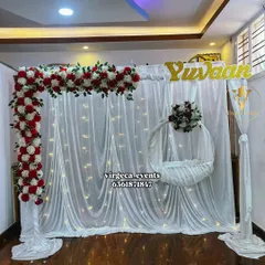 A simple and elegant Naming Ceremony backdrop with white drapes, fairy lights, and a red and white floral arch.