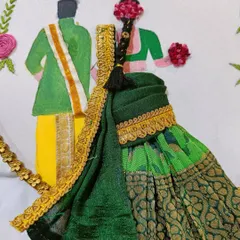 A close-up of the traditional couple hoop art, showing the detail in the miniature saree and the groom's dhoti. The floral hair accessory is also embroidered.