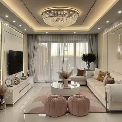 A classic, grand crystal chandelier serves as the centerpiece in this elegant living room. It is complemented by recessed spotlights and cove lighting around the perimeter of the ceiling for a soft, ambient glow.