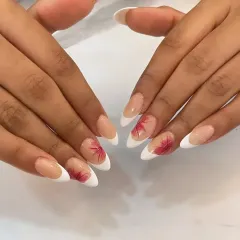 A full view of the elegant French manicure with hand-painted red leaves. This custom art adds a unique and personal element to a timeless style.
