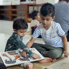 Continuing the story, the older brother now guides his sister through an animal puzzle. This is peer learning in its most natural form, building confidence in the older child and providing comfort and guidance to the younger one.