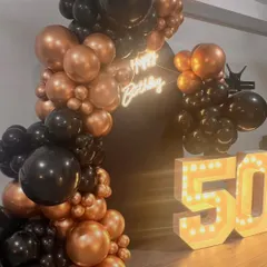 A straight-on shot showcasing the complete 50th birthday setup. The balance between the glowing numbers, the neon sign, and the balloon arrangement creates a visually appealing and photo-ready scene.