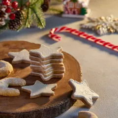 A lovely shot of star-shaped and crescent Christmas cookies on a rustic wooden board. The soft, warm lighting and festive decorations in the background create a gentle and inviting holiday mood for this Marriott Bonvoy shoot.