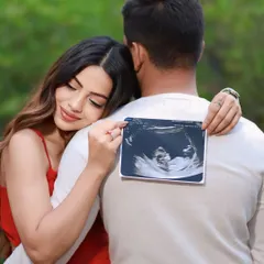 A sweet and creative announcement idea. The mom-to-be leans on her partner's back, holding the sonogram photo as a symbol of the little one who will soon join them.
